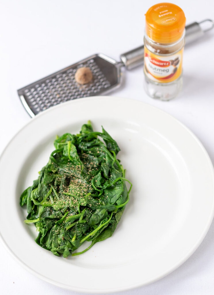 Spinach on a white plate garnished with grated nutmeg.