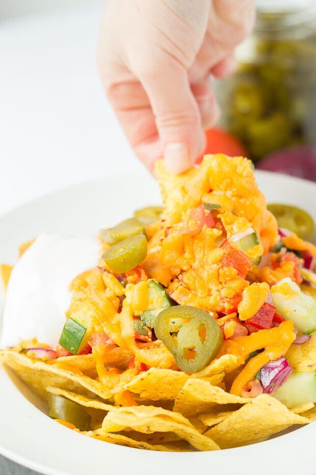 A hand pulling some nachos covered with melted cheese. 