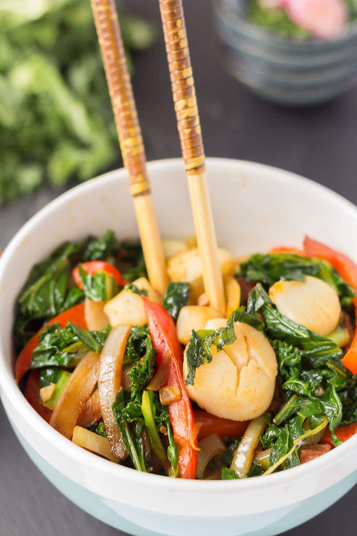 A bowl of chorizo scallop and kale stir fry with chopsticks in.