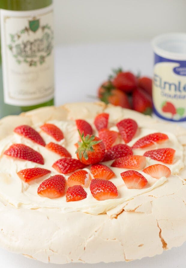 Easy strawberry pavlova topped with cream and decorated with strawberry halves.