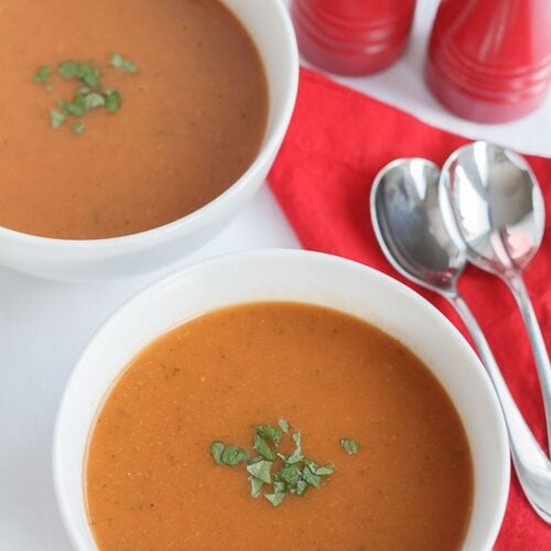 Birds eye view of two bowls of tomato and courgette soup alongside a napkin, two spoons and salt and pepper cellars.