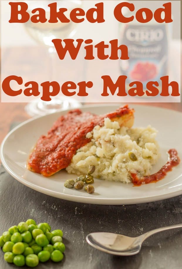Baked cod with caper mash served on a plate with a spoon and serving of peas at the front.