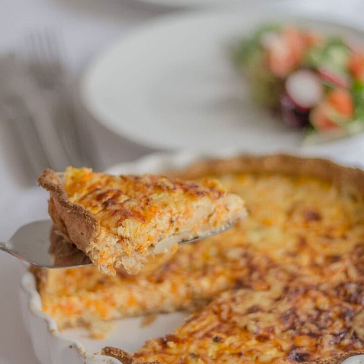 A slice of carrot and quark quiche being lifted out of a quiche dish.