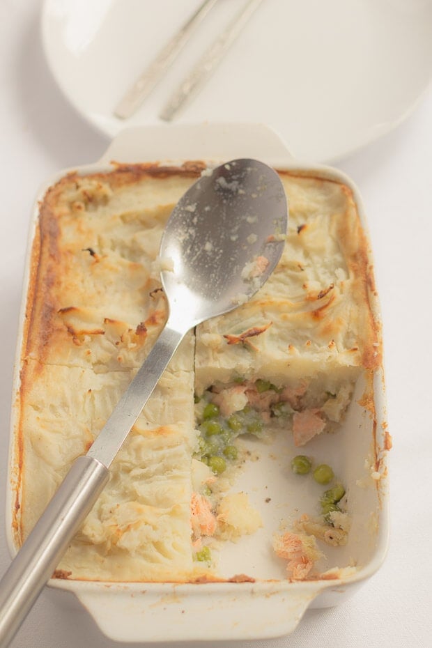 Creamy healthy fish pie with a quarter portion taken out and a spoon resting on top.