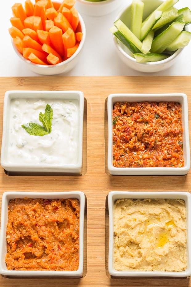 4 dishes of different kinds of low fat dip with baton carrots and cucumber.