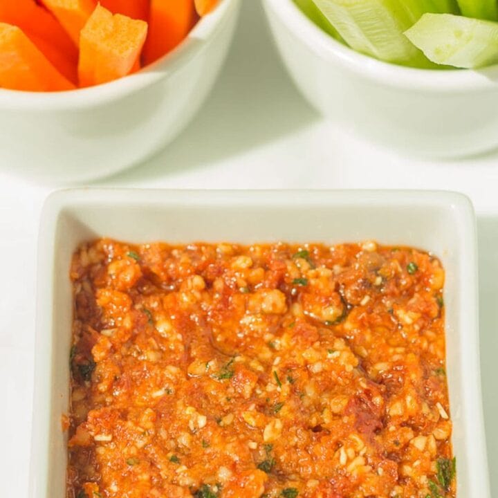 Low fat red pesto dip in a square dish with carrot and celery batons in the background.