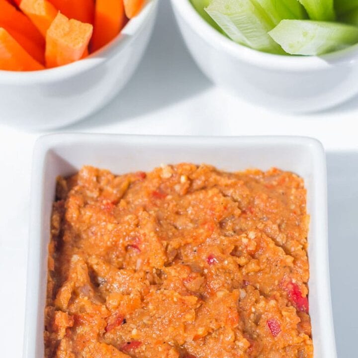 Low fat roasted red pepper dip in a white square serving dish with batton carrots and celery in the background.
