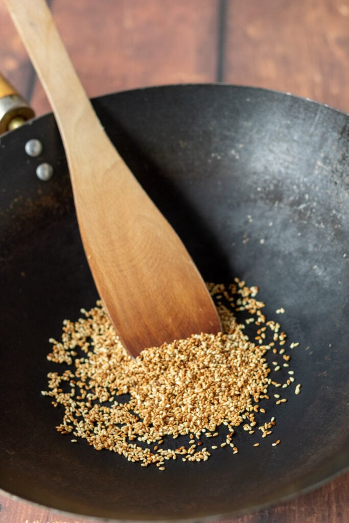 Sesame seeds being dry-fried until golden brown in a wok.