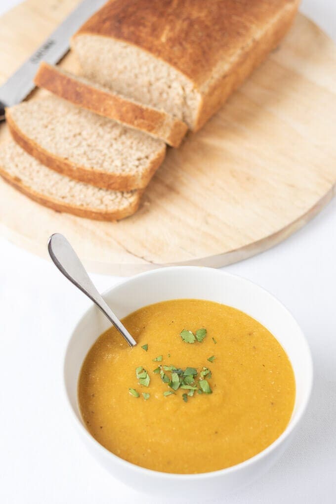 carrot and lentil soup in a bowl with sliced bread on a chopping board behind it