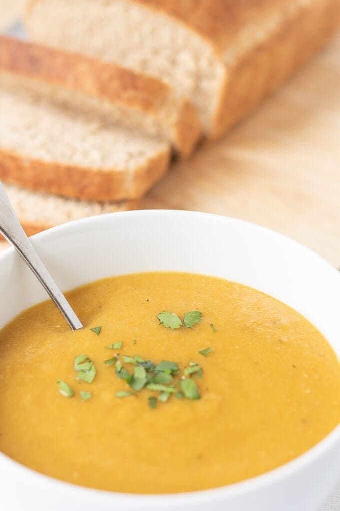 Close up of carrot and lentil soup with sliced bread on a board behind.