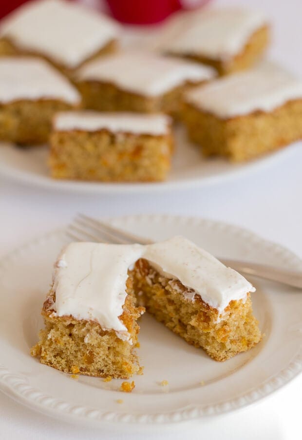 A slice of orange and apricot tray bake cut in half on a plate with a fork.