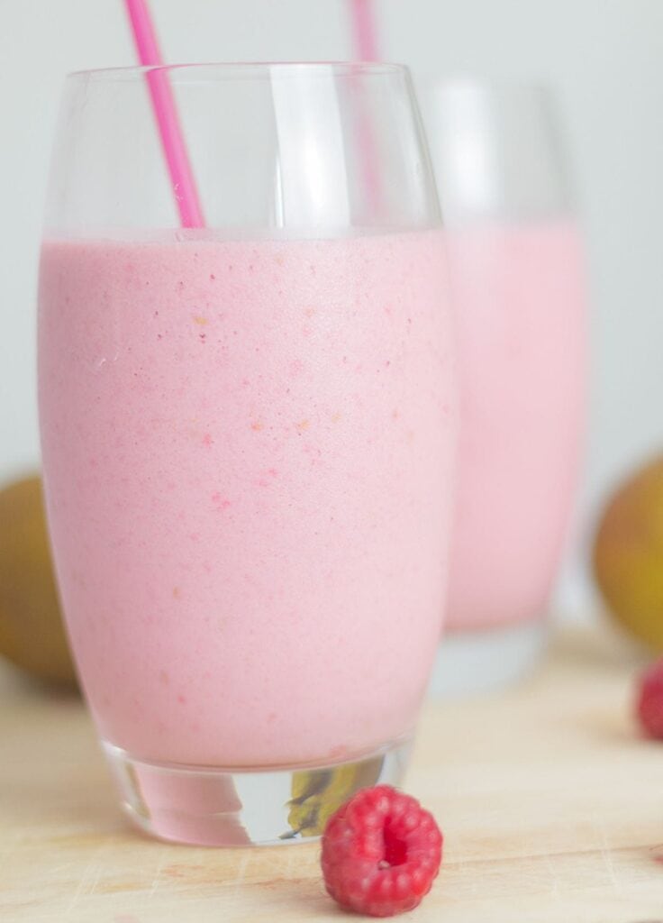 Two glasses of raspberry and pear smoothie one in front of the other with straws in.