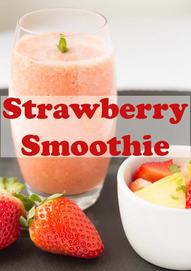 A glass of strawberry sunrise smoothie on a black slate. Pin title through the middle of the picture.