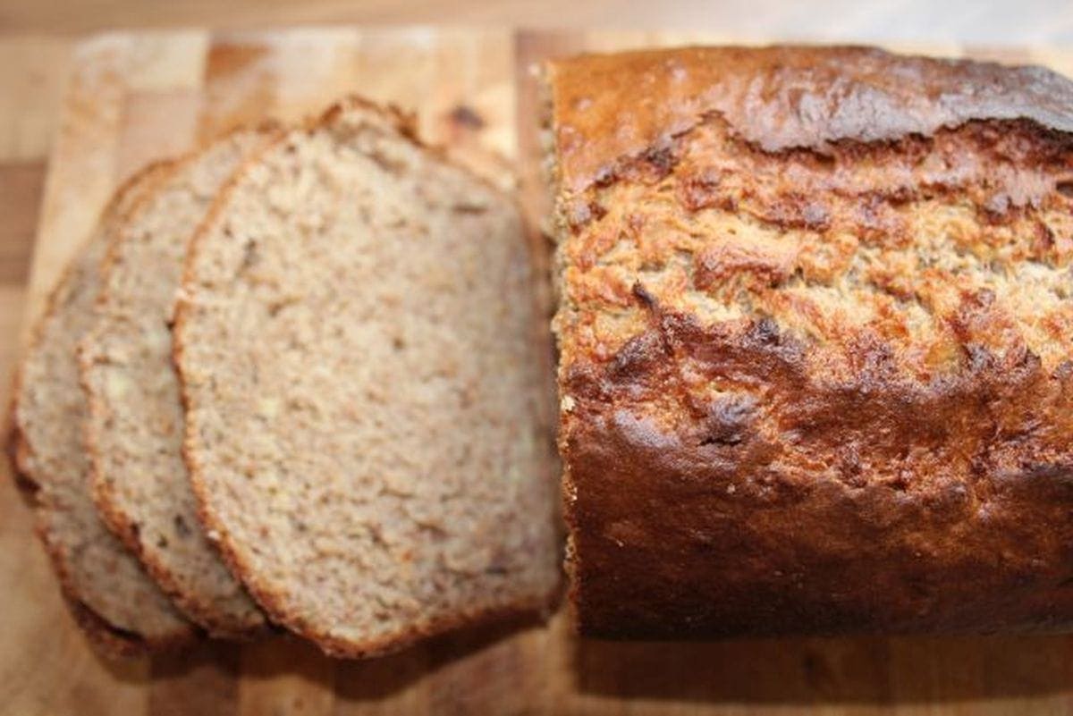 A loaf of banana bread on a chopping board with 3 slices cut off.