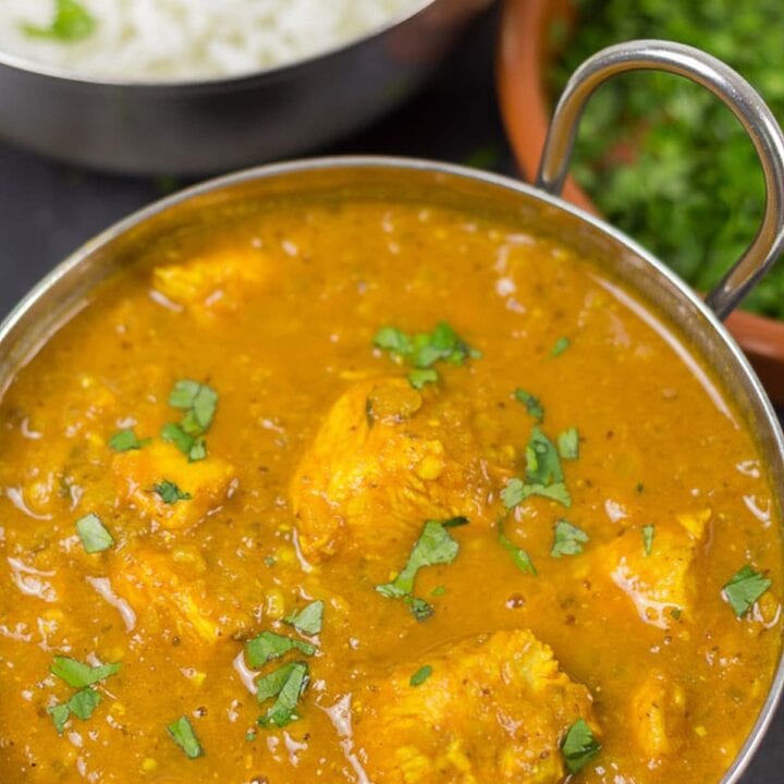 A balti dish of chicken vindaloo, garnished with chopped coriander. A rice dish and a dish of coriander in the background.