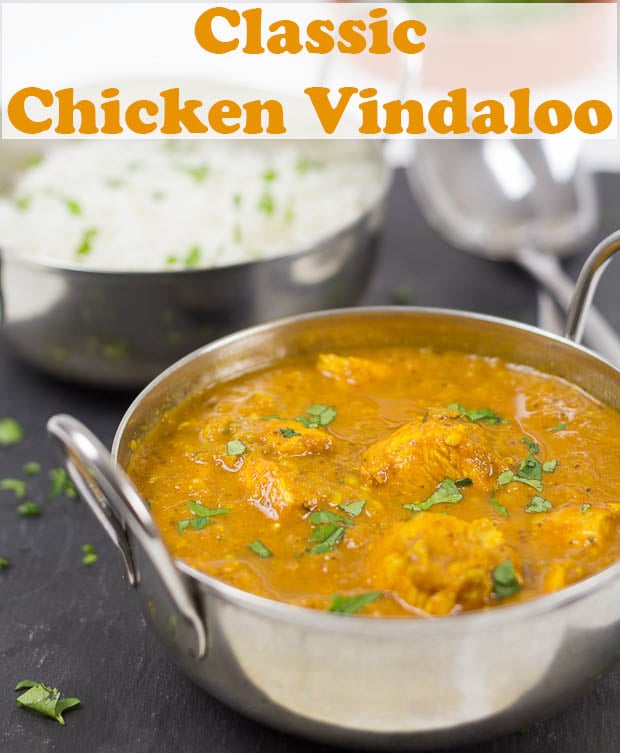 Classic chicken vindaloo in a balti dish with a balti dish of basmati rice in the background and two serving spoons.