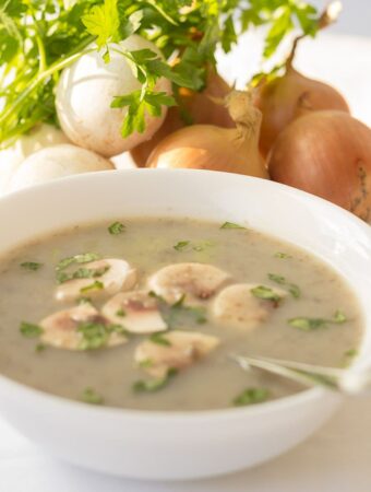 A bowl of creamy mushroom soup without the cream. Garnished with chopped mushroom and parlsey.