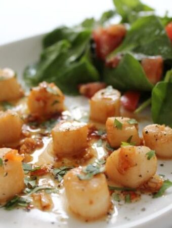 Scallops with chilli and lime served on a white plater serving dish with a green salad.