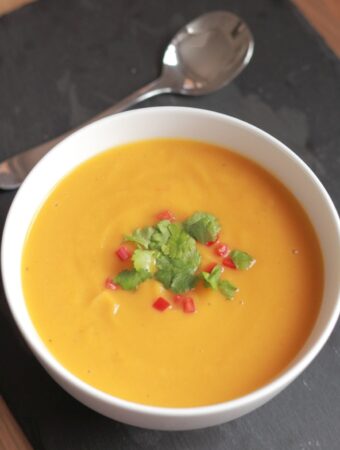 A bowl of sweet potato garlic and chilli soup garnished with chopped red chillies and coriander.