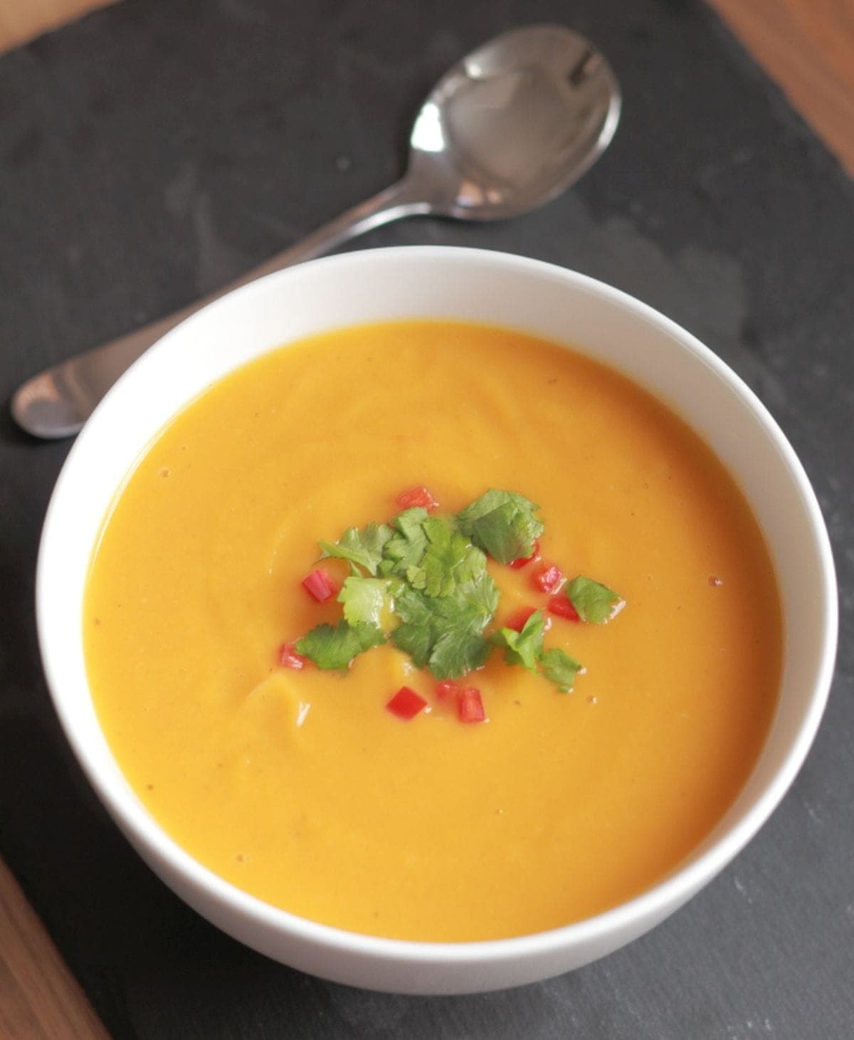 A bowl of sweet potato garlic and chilli soup garnished with chopped red chillies and coriander.