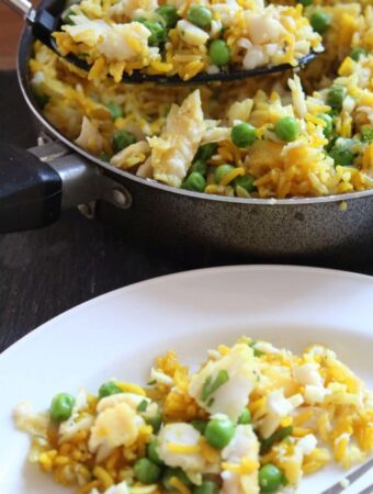 A large spoonful of Kedgeree being lifted from the cooking pan onto a white plate with a fork on.