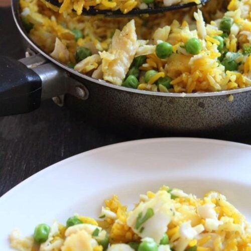 A large spoonful of Kedgeree being lifted from the cooking pan onto a white plate with a fork on.
