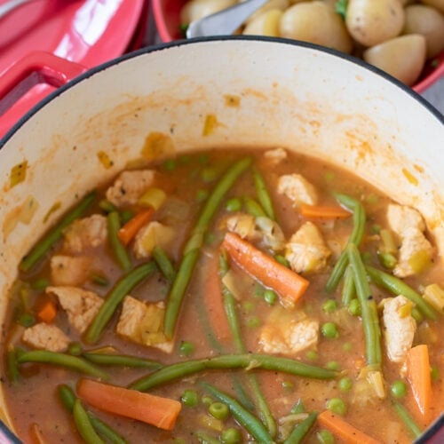 Low fat summer turkey stew cooked in a casserole pot. Bowl of baby potatoes and plates with two forks on in the background.