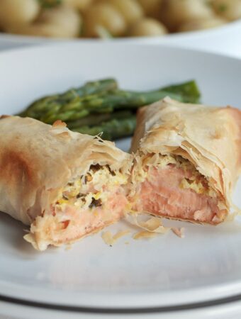A salmon filo parcel cut in half on a plate with asparagus in the background.