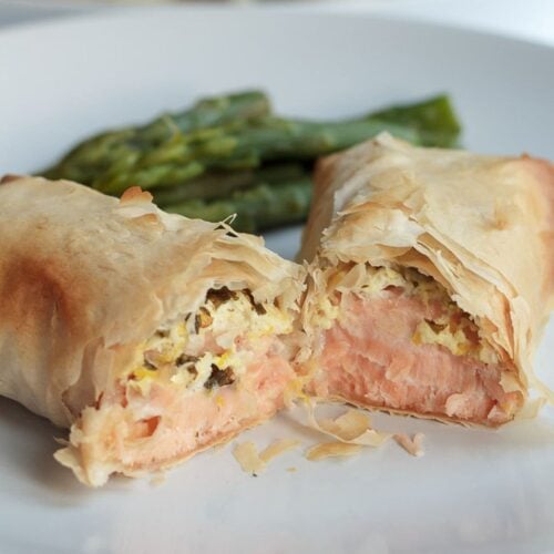 A salmon filo parcel cut in half on a plate with asparagus in the background.