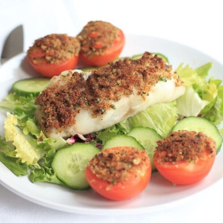 Grilled fish provencal served on top of a iceberg lettuce salad with sliced tomatoes.