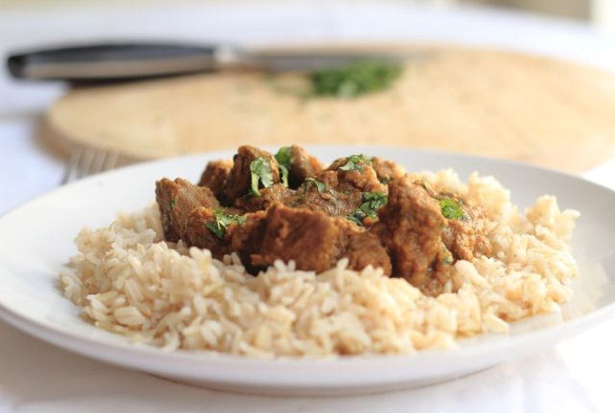 Close up of a plate of lamb chilli curry served on a bed of rice.