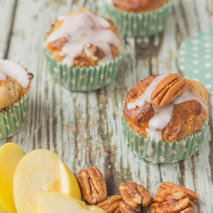 A selection of apple and pecan muffins in the background and some sliced apple and pecan nuts in the foreground.