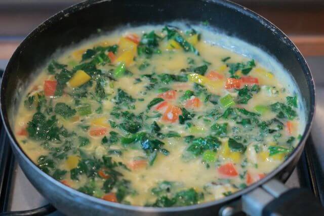 A poaching pan of kale and pepper frittata with the egg and kale just having been added to the peppers.