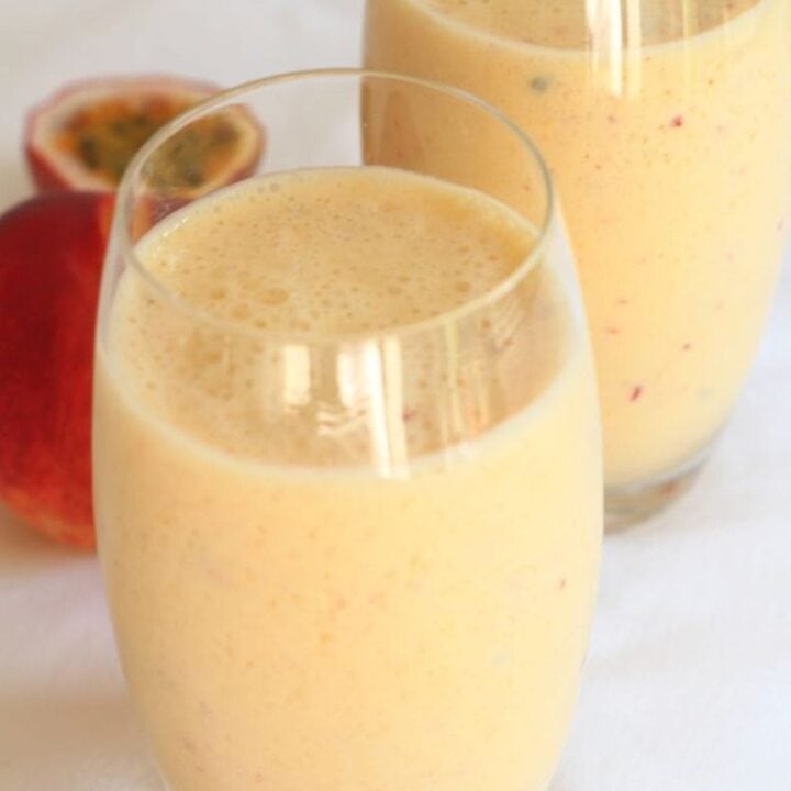 Two glasses of mango peach and passion fruit smoothie with a passion fruit in the background.
