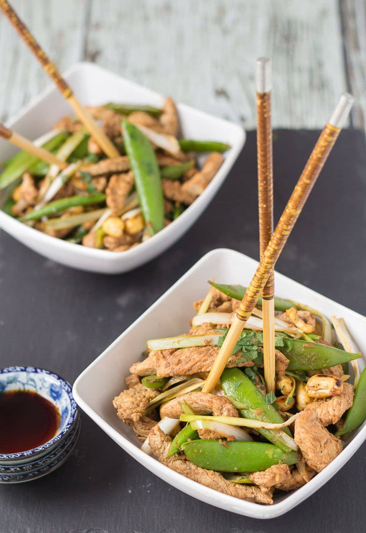 Two square bowls of turkey stir fry with sugar snap peas and chop sticks standing up in the bowls.