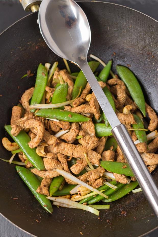 Birds eye view of a wok of cooked stir fry turkey with sugar snap peas and serving spoon resting over the top.