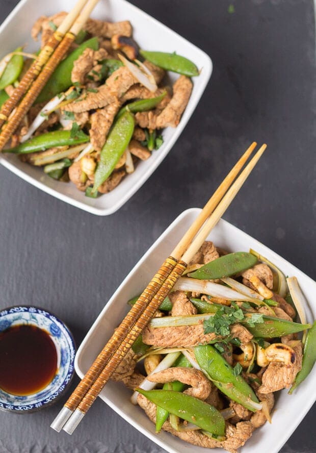 Two square bowls of stir fry turkey with sugar snap peas and chop sticks resting on the side of each bowl.