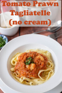 Creamless tomato prawn tagliatelle served in a white pasta dish garnished with chopped parsley. Pin title text overlay at top.