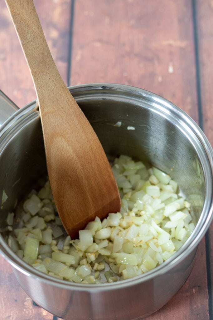 Onion and garlic being sauteed in a saucepan.