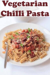 A plate of vegetarian chilli pasta with a fork in. Pin title text overlay at top.