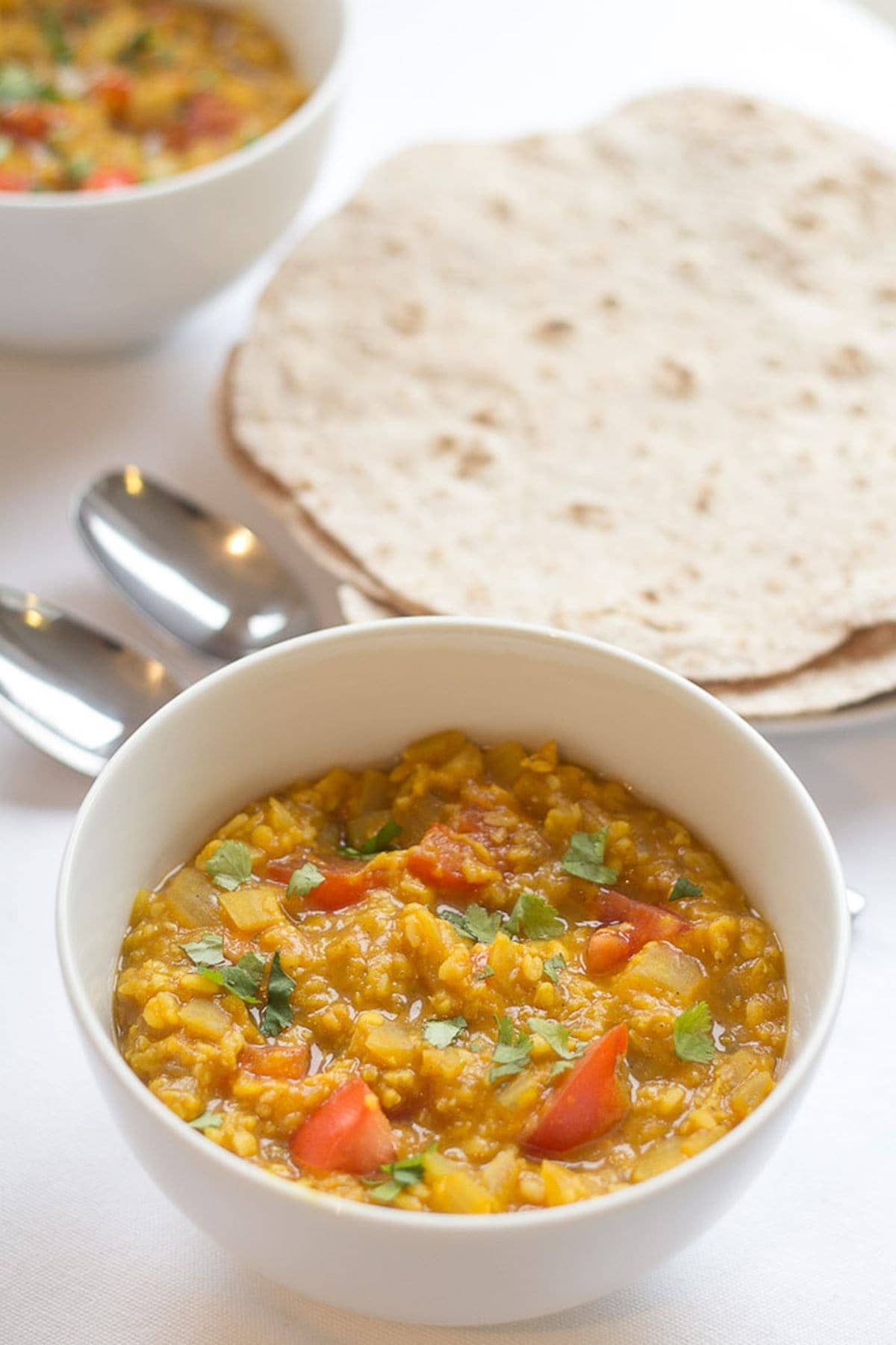 A bowl of moong dall dahl with naan breads in the background and spoons in between.