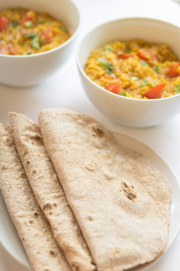 A plate of three folded in half naan breads with two bowls of Mung Bean (Moong Dall) Dahl in the background
