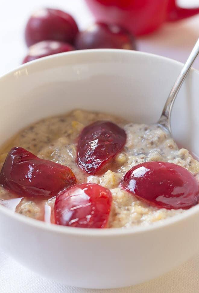 A bowl of spiced plum millet porridge with 4 plum halves on top and spoon in.