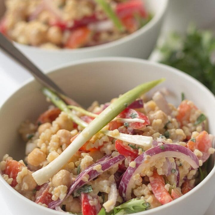 Two bowls of bulgur chickpea salad one in front of the other garnished with spring onions.