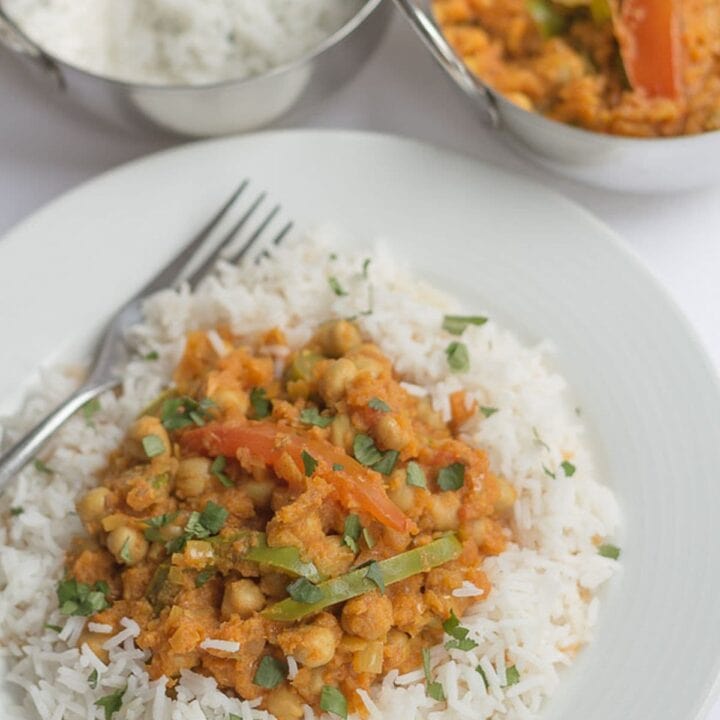 A plate of healthy chickpea curry garnished with chopped coriander. Two balti dishes of rice and more curry in the background.