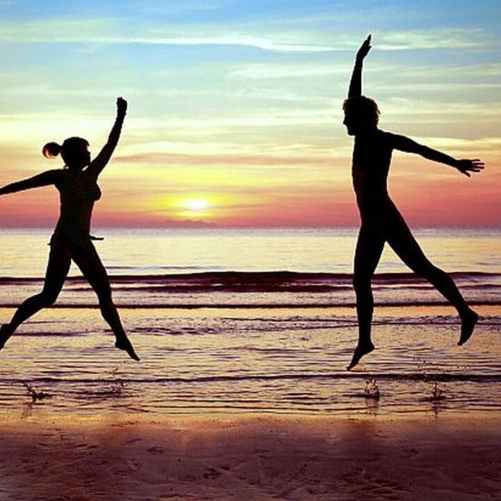 Healthy body healthy mind image. Two people jumping on a beach.