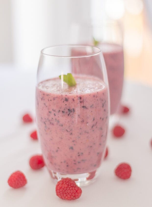 A glass of blueberry apple smoothie with raspberries as decoration around the base.