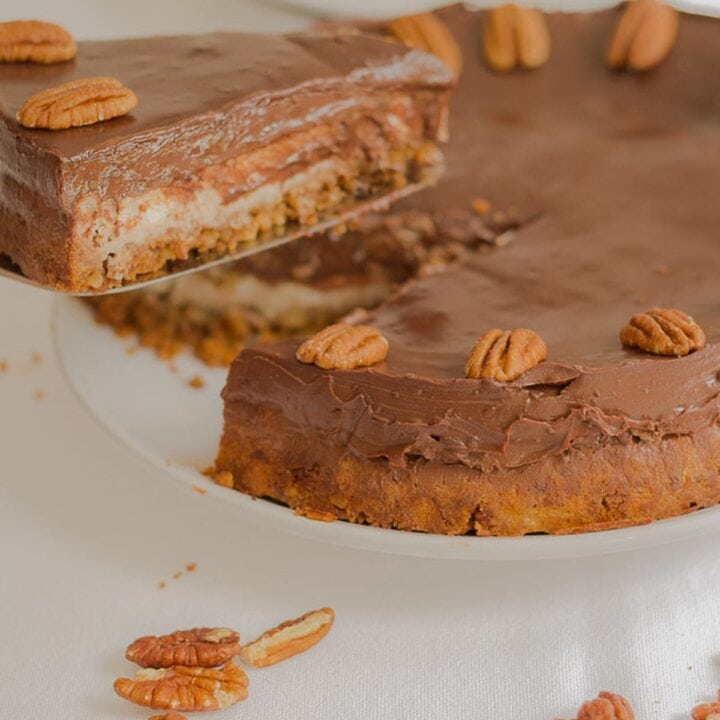 Chocolate ganache cheesecake with a slice being lifted out. Pecan nuts decorated around the cheesecake.