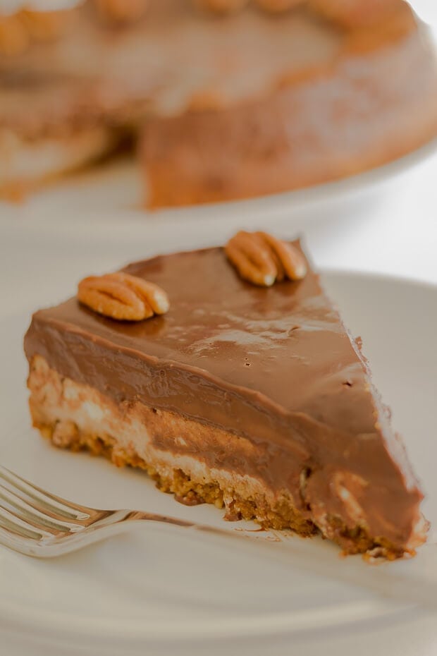 A slice of chocolate ganache cheesecake on a plate decorated with pecan nuts and a fork beside.