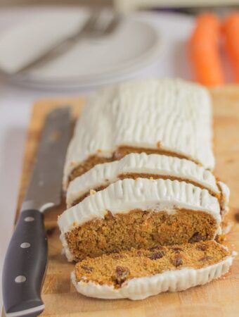 Gluten free carrot and sultata cake on a chopping board. Three slices cut off with a carving knife to the right.